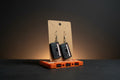 Black retro cassette tape earrings on display card resting on an orange cassette tape